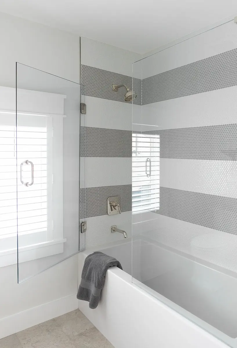 Bathroom with freestanding tub, glass shower enclosure, gray and white striped tiles, and white window.
