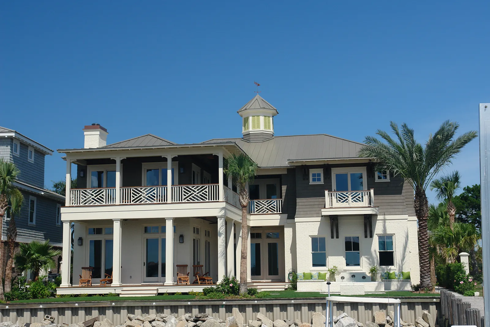 Front exterior view of a house with balcony, turret, palm trees, and stone wall.