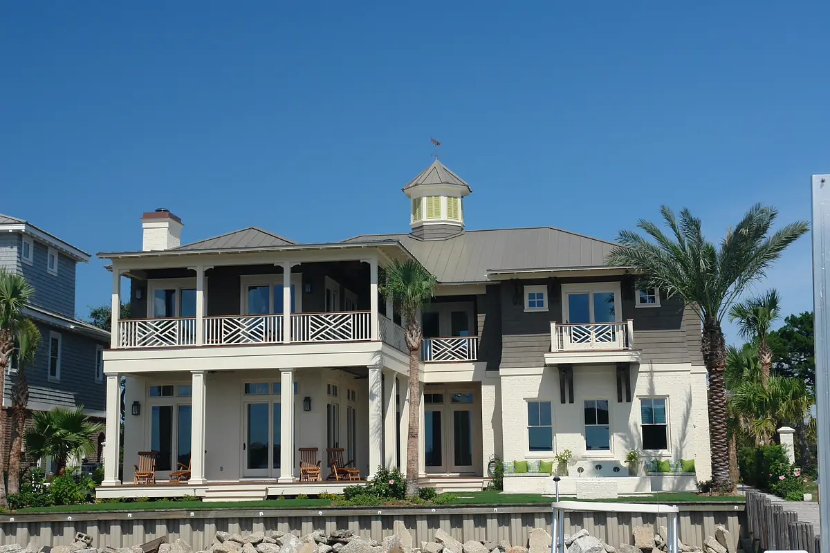 Front exterior view of a house with balcony, turret, palm trees, and stone wall.