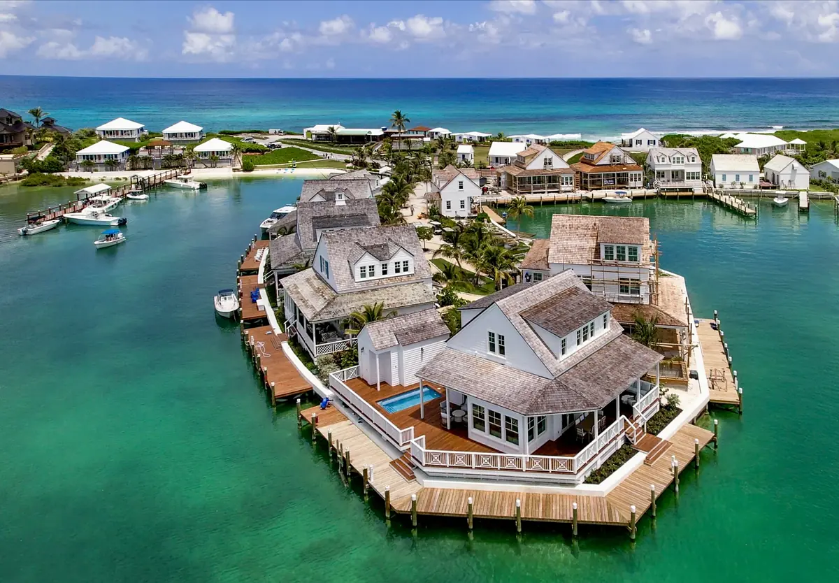 Waterfront property exterior view with multiple houses, wooden decks, palm trees, and ocean backdrop.