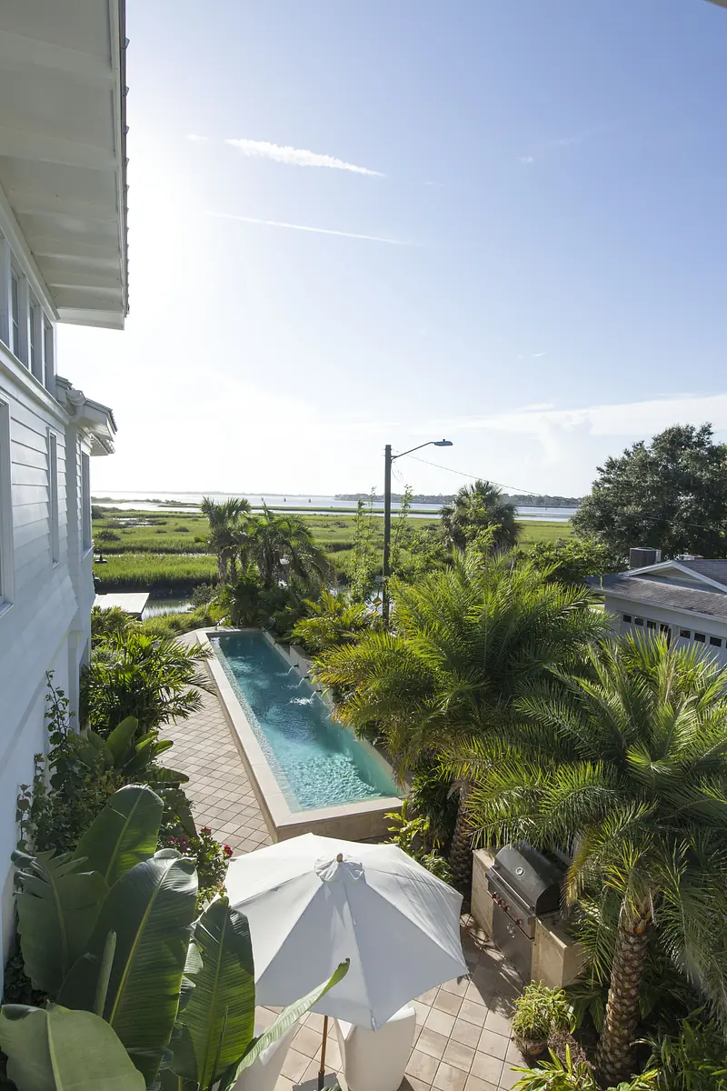 Exterior area with pool, tropical landscaping, patio with umbrella, and grill overlooking water.