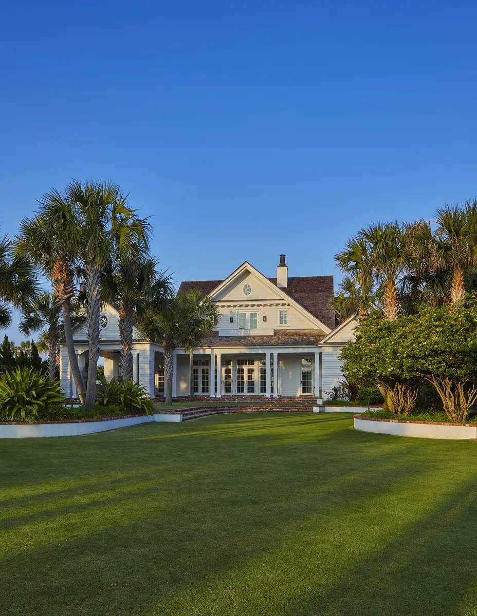 Front exterior of a house with porch, columns, palm trees, and landscaped yard.