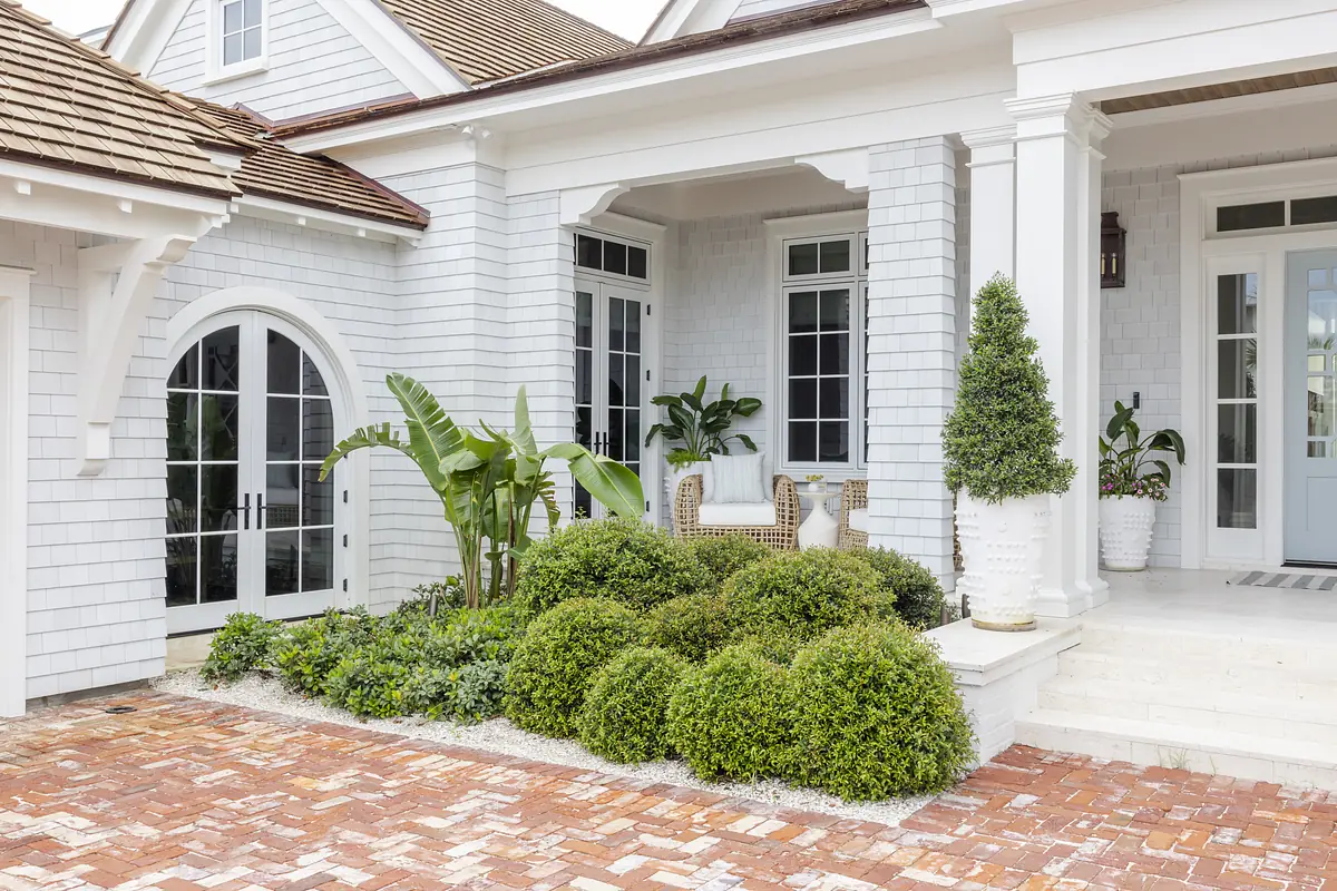 Exterior front view of a house with brick pathway, white siding, and manicured shrubs.