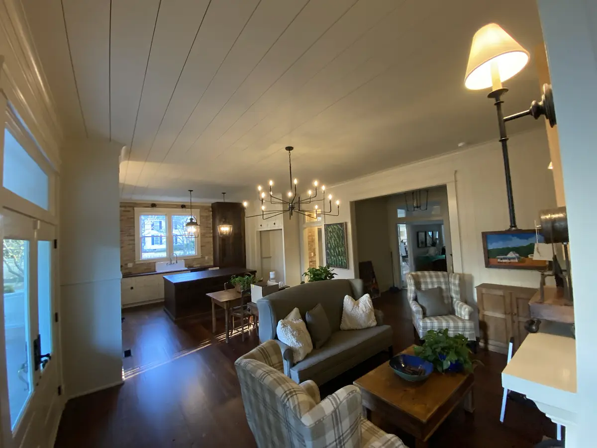 Living room with gray sofa, plaid armchairs, wooden coffee table, and dining area in the background.