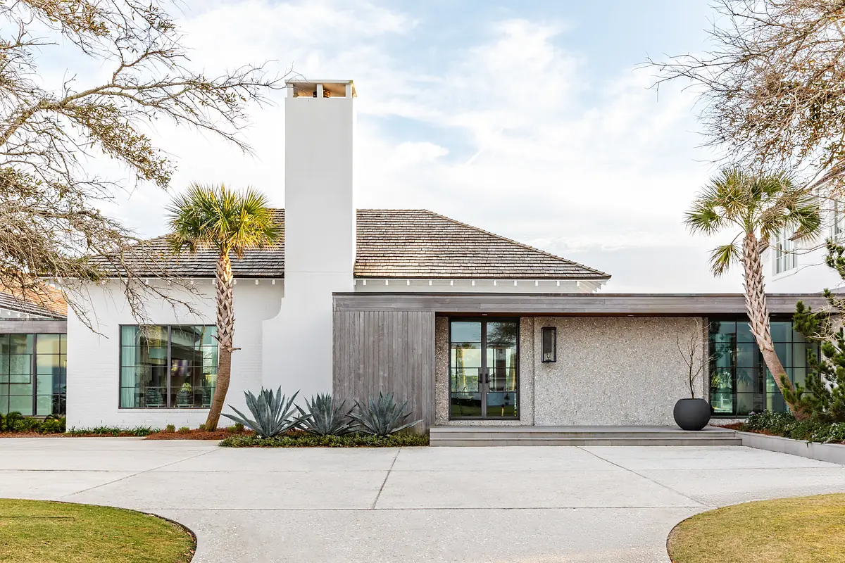 Front exterior of house with white wall, stone facade, wood panel, large windows, and palm trees.