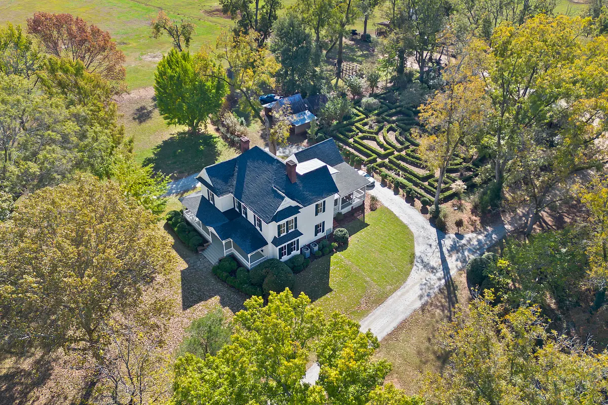 Exterior view of a house with gables, white siding, a dark roof, flower beds, and gravel driveway.