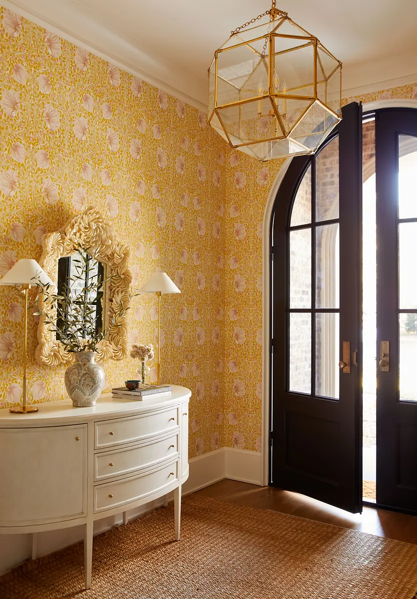 Foyer with white console table, decorative mirror, yellow floral wallpaper, and arched black doors.