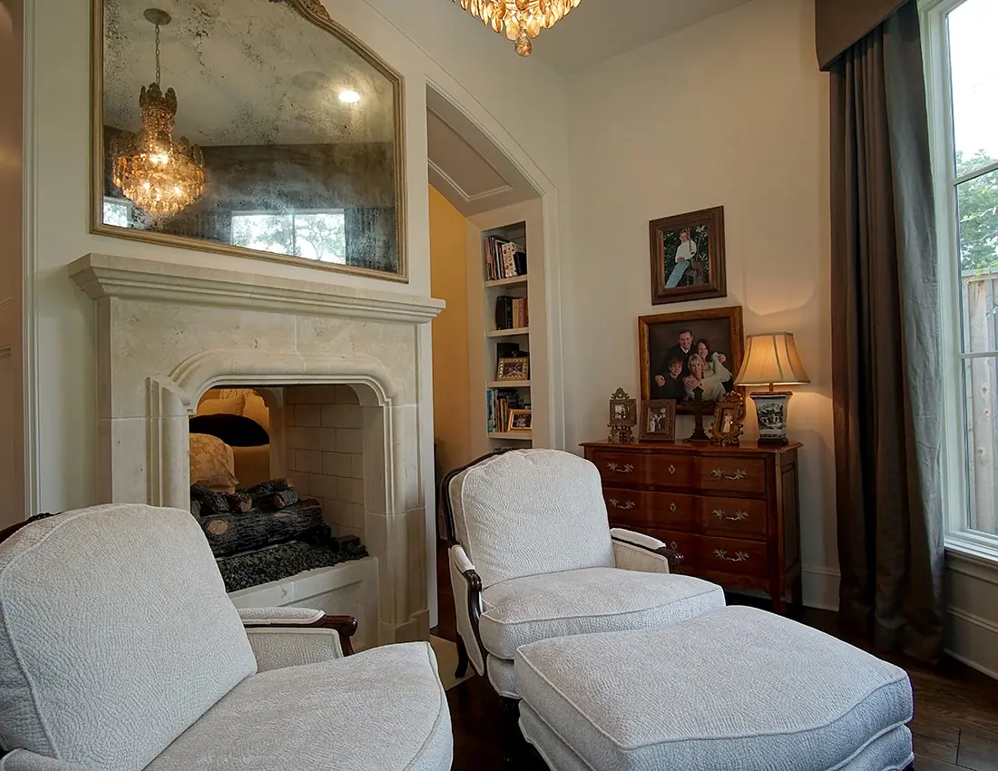 Living room with beige armchairs, stone fireplace, wooden dresser, and bookshelves with natural light.