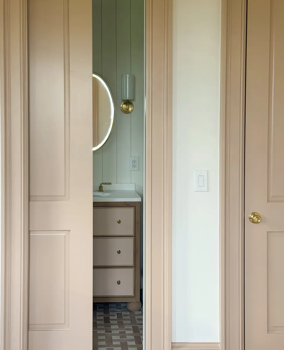 Bathroom with beige paneled walls, round mirror, white vanity, and tiled floor.