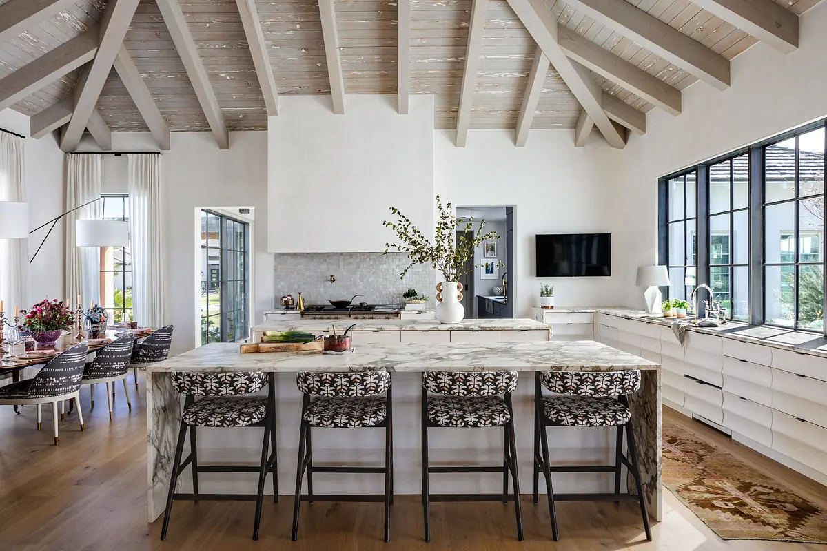 Kitchen with marble island, bar stools, minimalist cabinetry, stove, sink, and large windows with natural light.