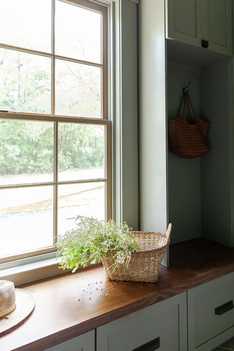 Mudroom with wooden countertop, basket of greenery, large window, and built-in cabinetry