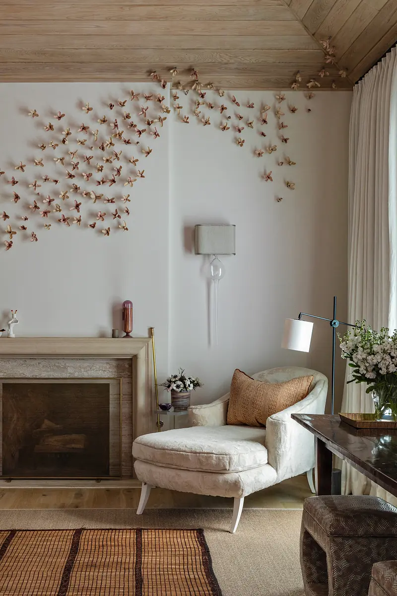 Living room with white armchair, side table, decorative butterflies, stone fireplace, and a wooden coffee table.