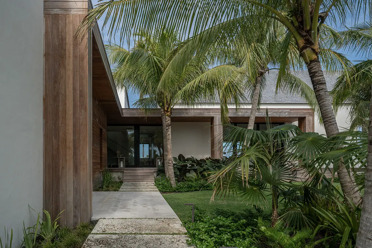Exterior front area with concrete pathway, palm trees, shrubs, and a modern building with wooden facade and large windows.