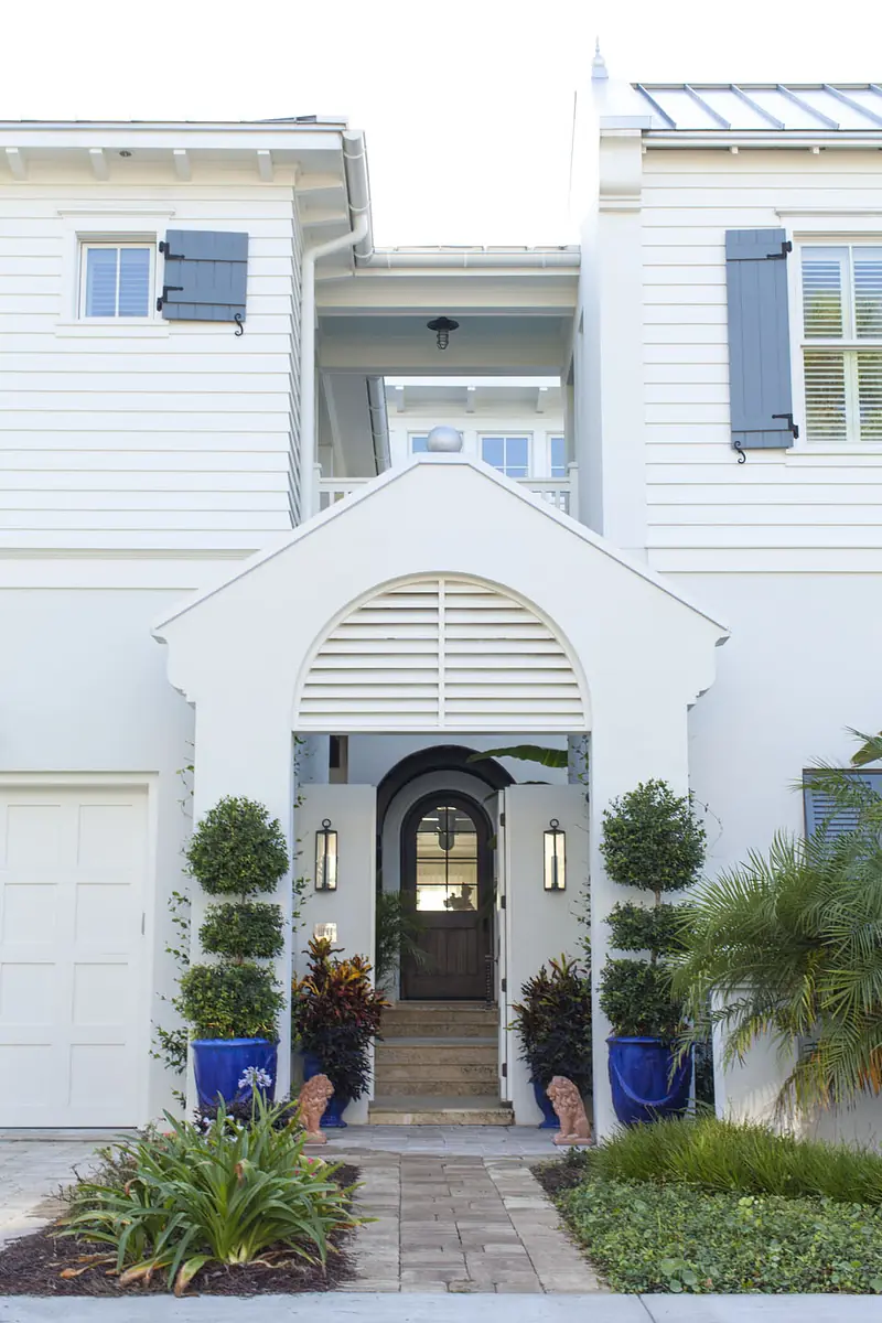 Exterior front with white house, blue shutters, archway, wooden door, and landscaped pathway.
