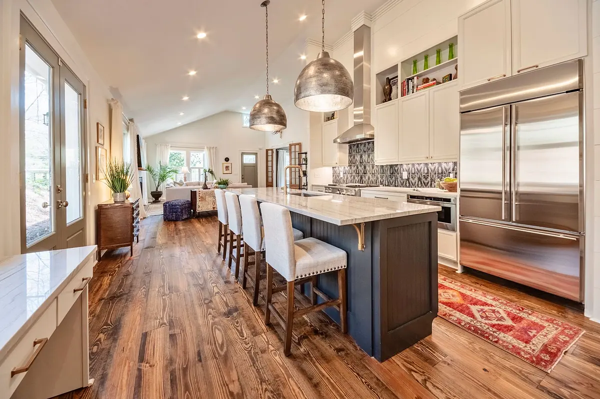 Kitchen with island, bar stools, stainless steel appliances, light wood cabinetry, and natural light from windows.
