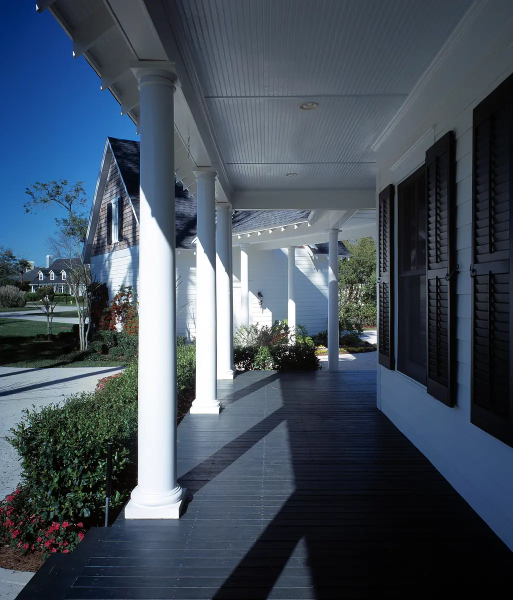 Exterior front featuring covered porch with columns, dark flooring, plants, windows, and gabled roof.