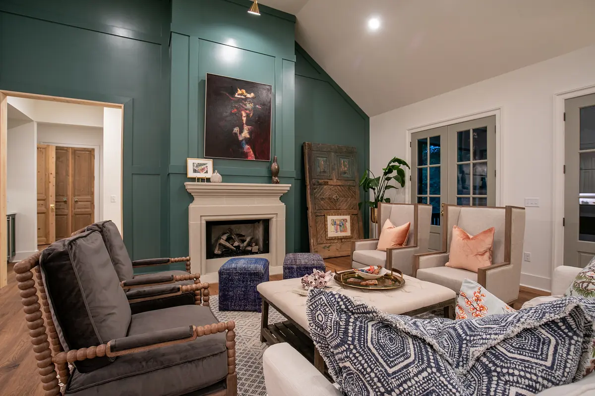 Living room with gray armchairs, coffee table, area rug, green feature wall, and white fireplace.