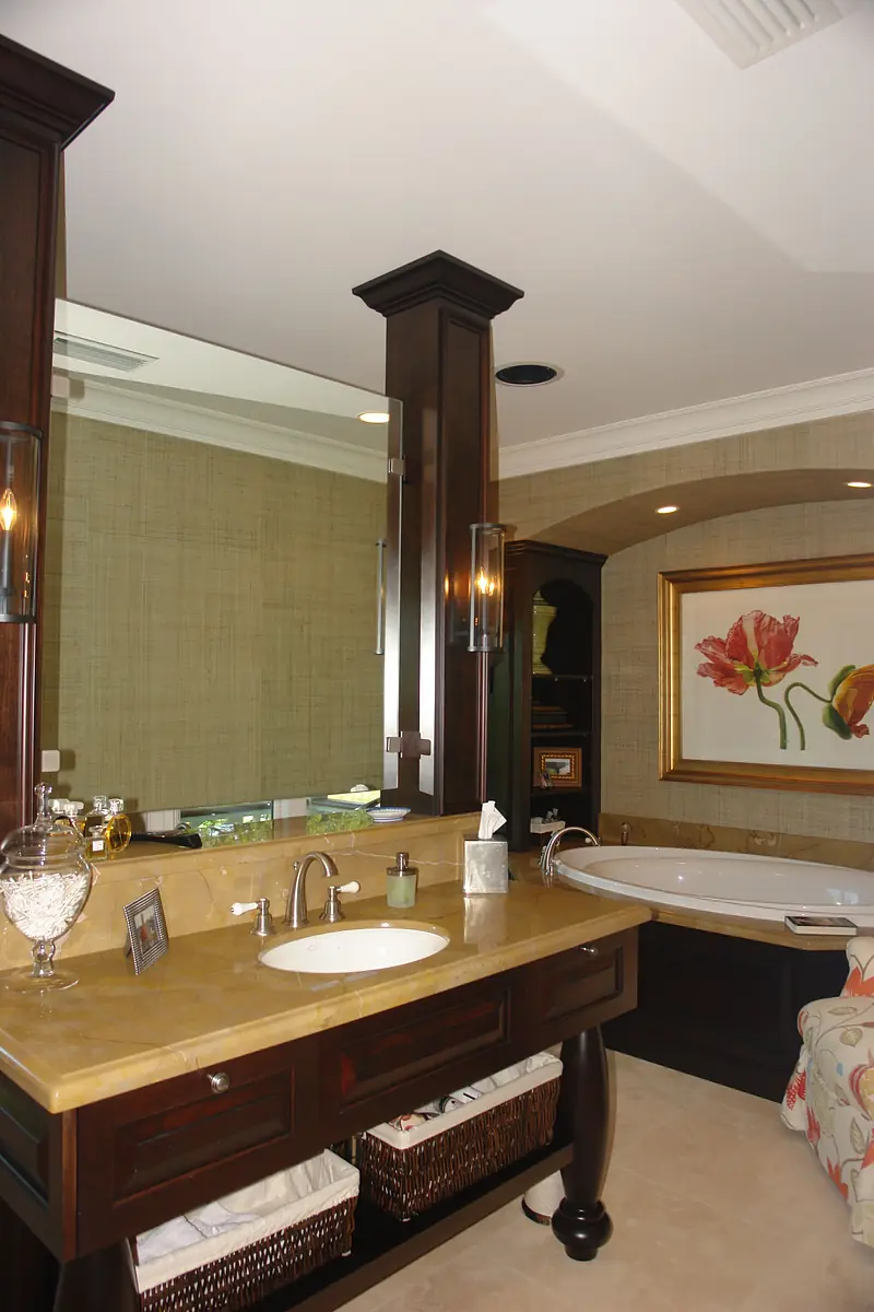 Bathroom with dark wood vanity, beige countertop, dual sinks, framed flower painting, and white bathtub.
