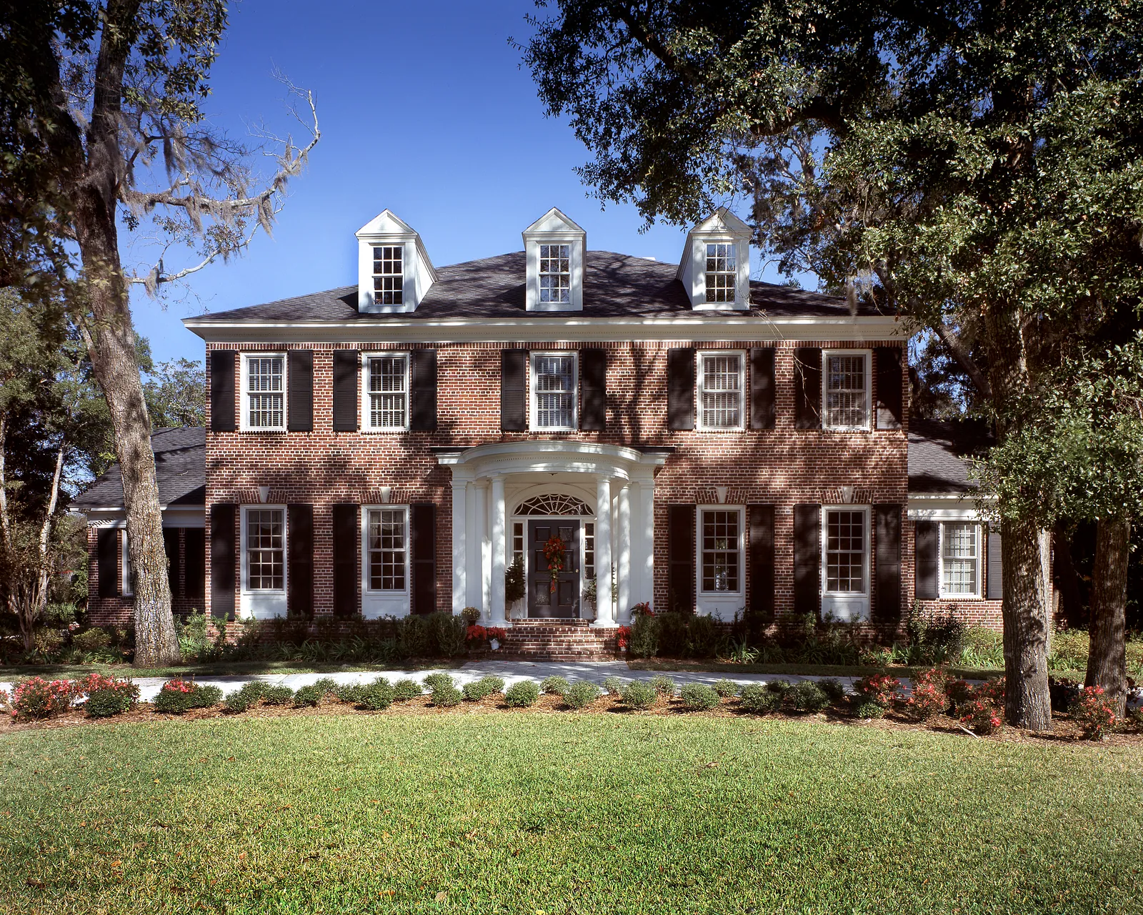 Exterior front view of a two-story brick home with central entrance and flower beds.