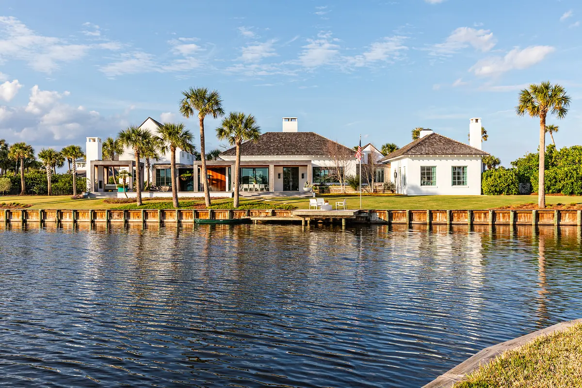 Waterfront property with three structures, wooden dock, palm trees, and grass landscape.