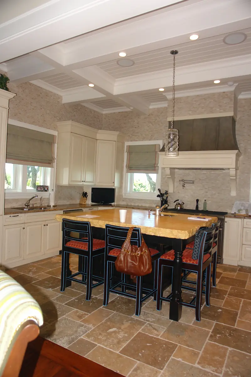 Kitchen with large island, white cabinets, stone tile flooring, and dual windows for natural light.