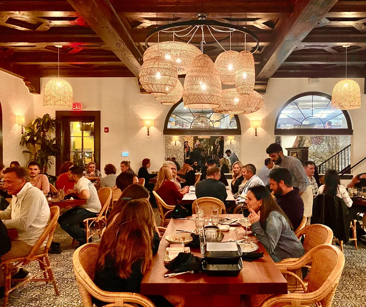 Dining room with wooden tables, woven chairs, pendant lights, and arched windows.