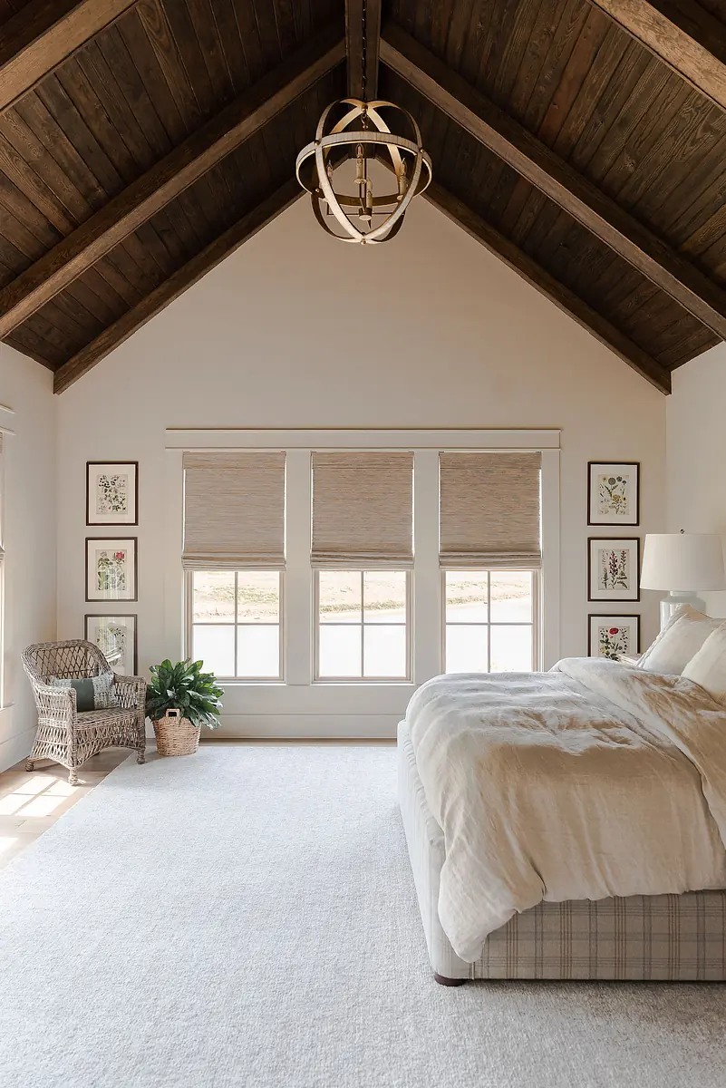 Bedroom with bed, wicker chair, area rug, windows, artwork, and vaulted wooden ceiling