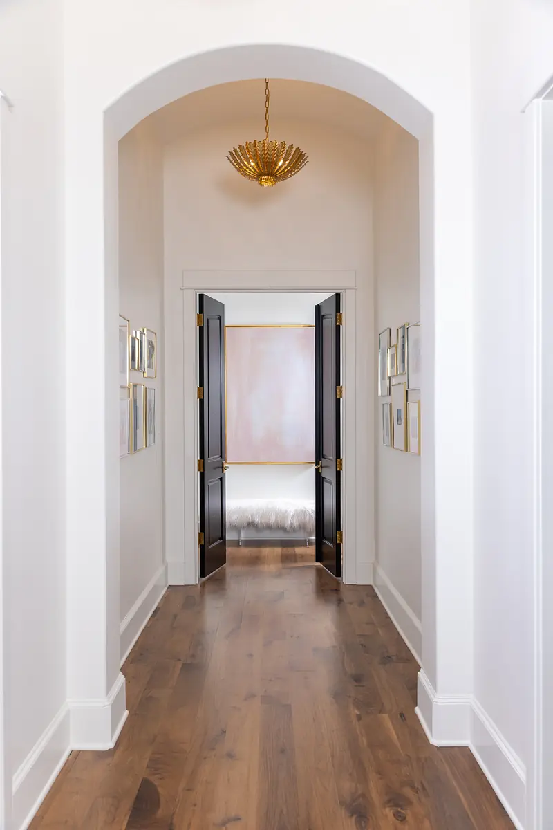 Hallway with black double doors, white walls, framed artworks, and wooden floor.