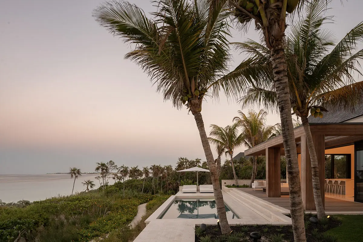 Exterior rear view with swimming pool, palm trees, landscaping, patio area, and ocean view at sunset