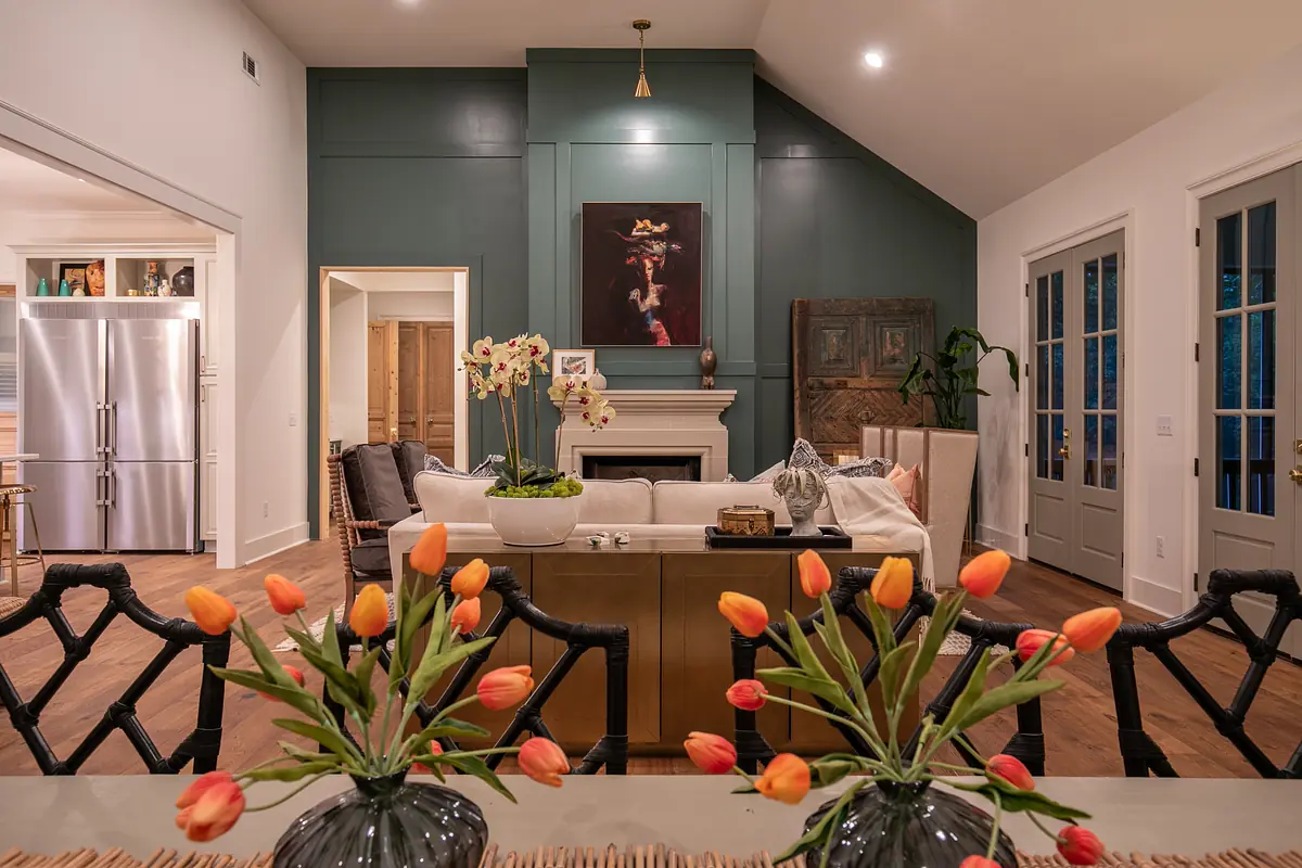 Living room with gray sectional sofa, white coffee table, orange tulip vases, green accent wall, and large windows.