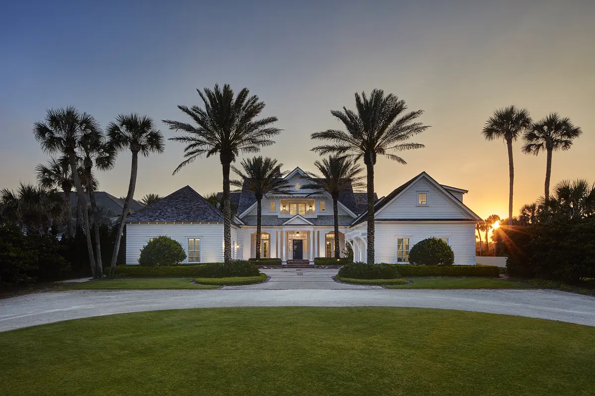 Front exterior of a house with central entryway, palm trees, and landscaped lawn.