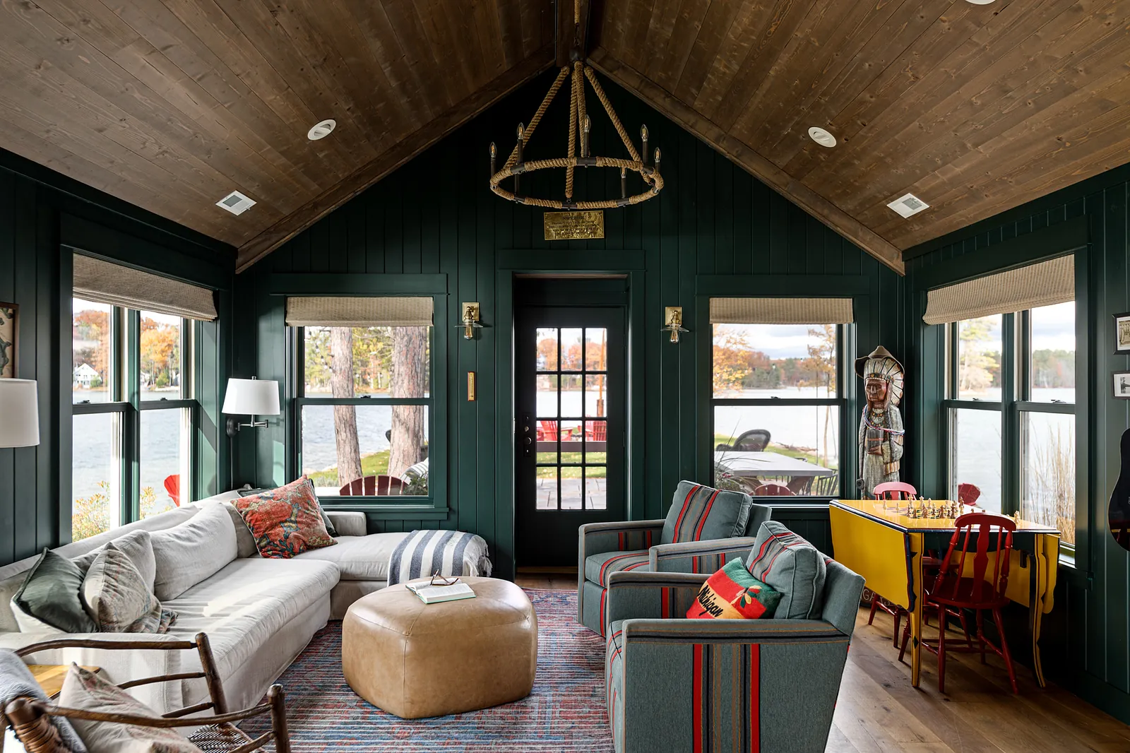 Living room featuring a white sectional, striped armchairs, round ottoman, dark green walls, and large windows.