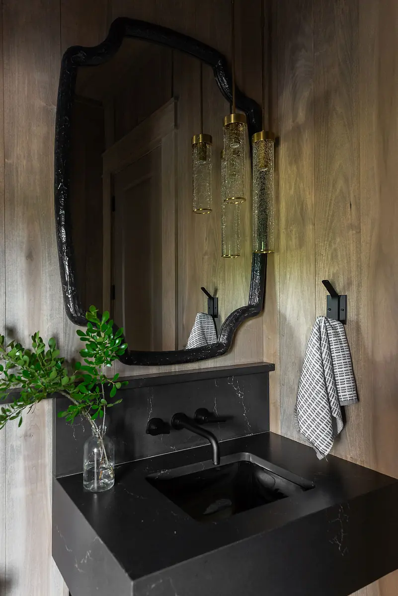 Powder room with black marble sink, large mirror, wooden paneling, and hanging pendant lights.