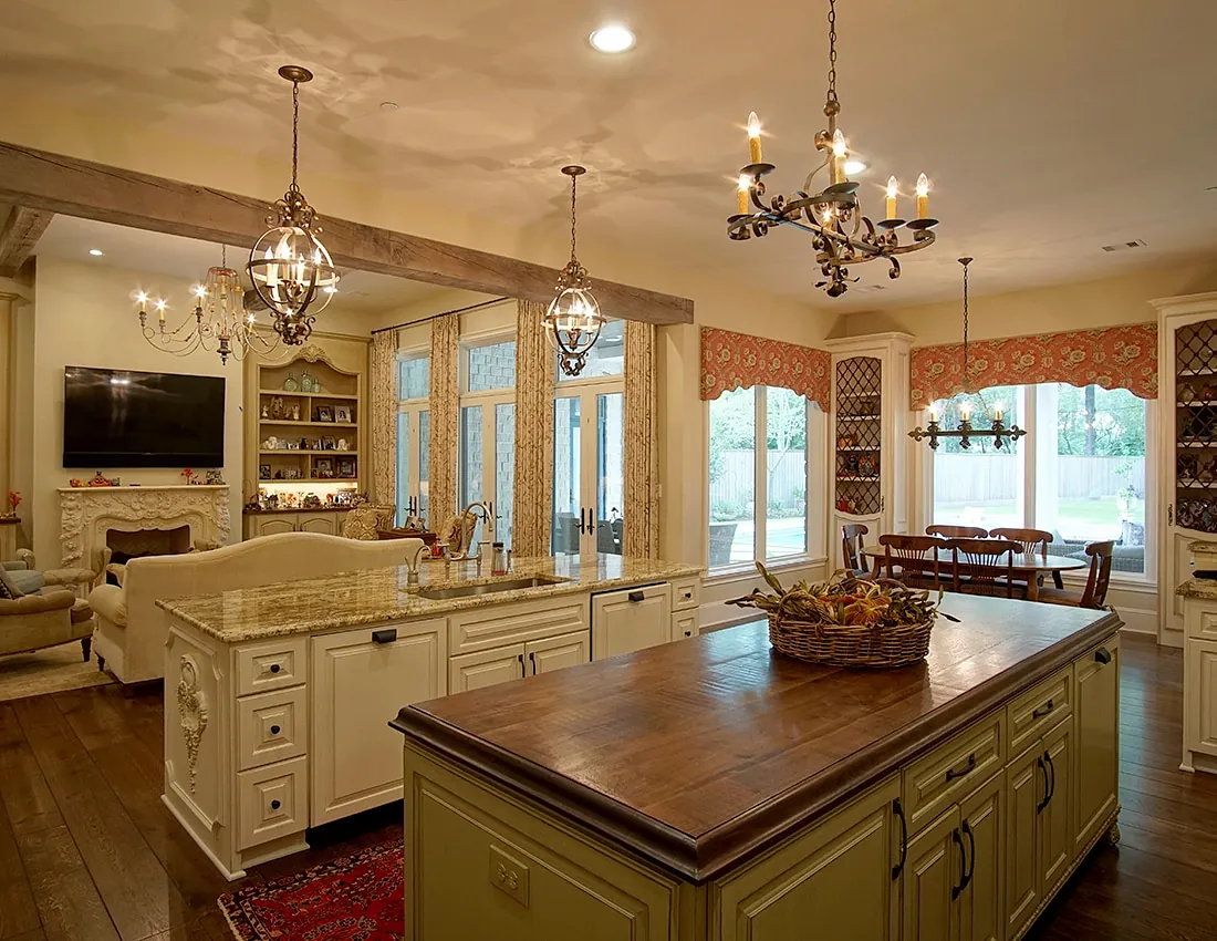 Kitchen with island, cream cabinetry, stone backsplash, chandeliers, and a dining table with chairs.