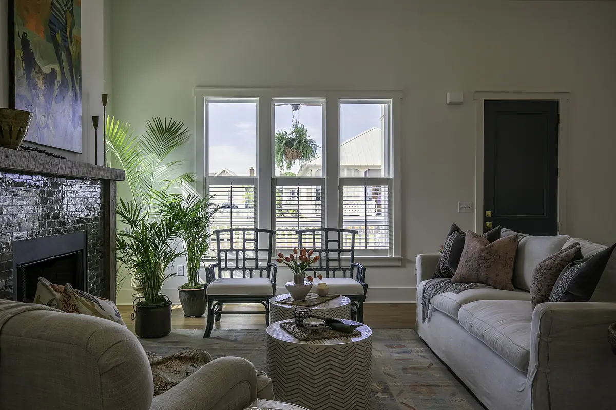 Living room with light sofa, patterned rug, coffee table, armchairs, large windows, and a fireplace.