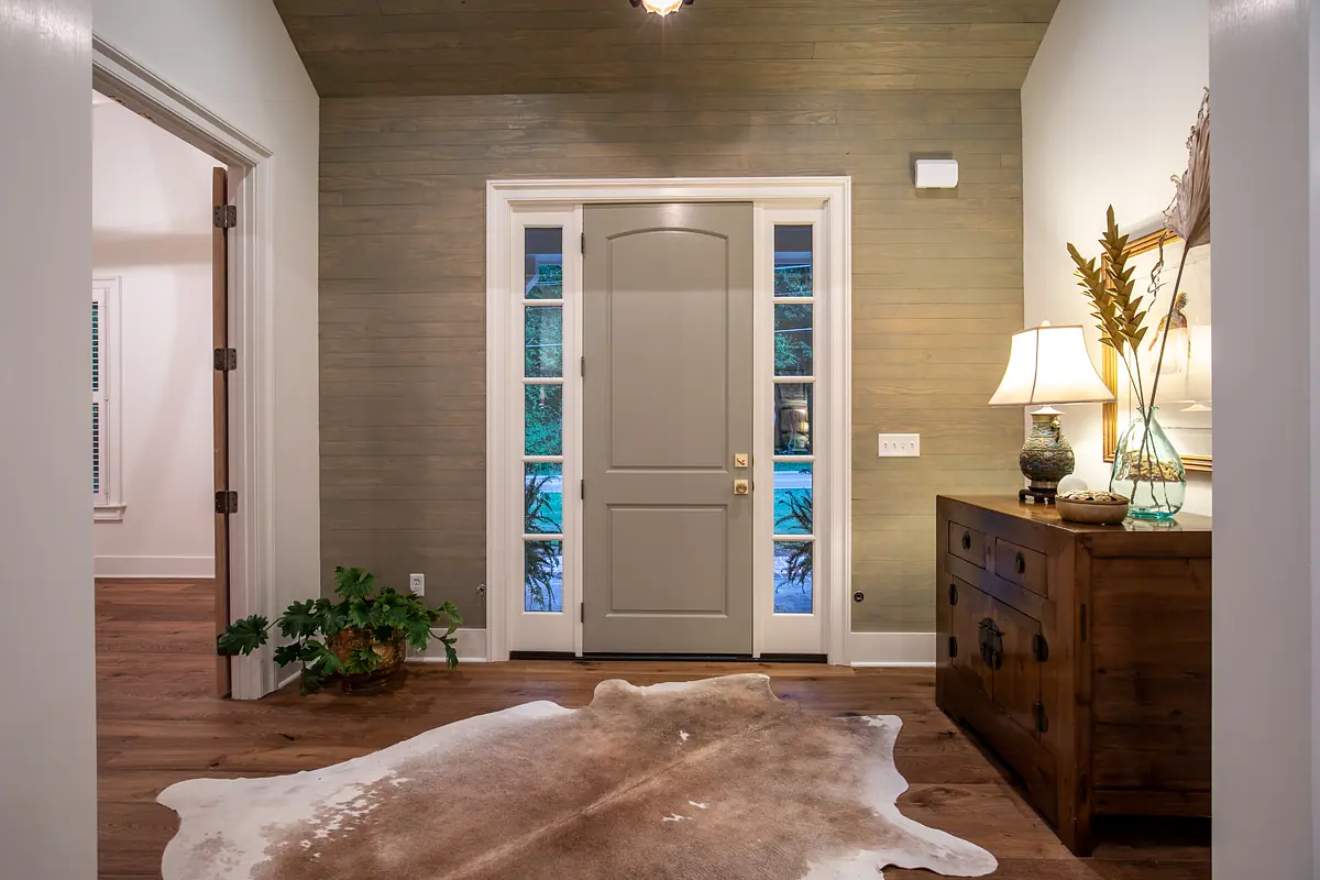 Foyer with wooden door, console table, lamp, plant, and cowhide rug.