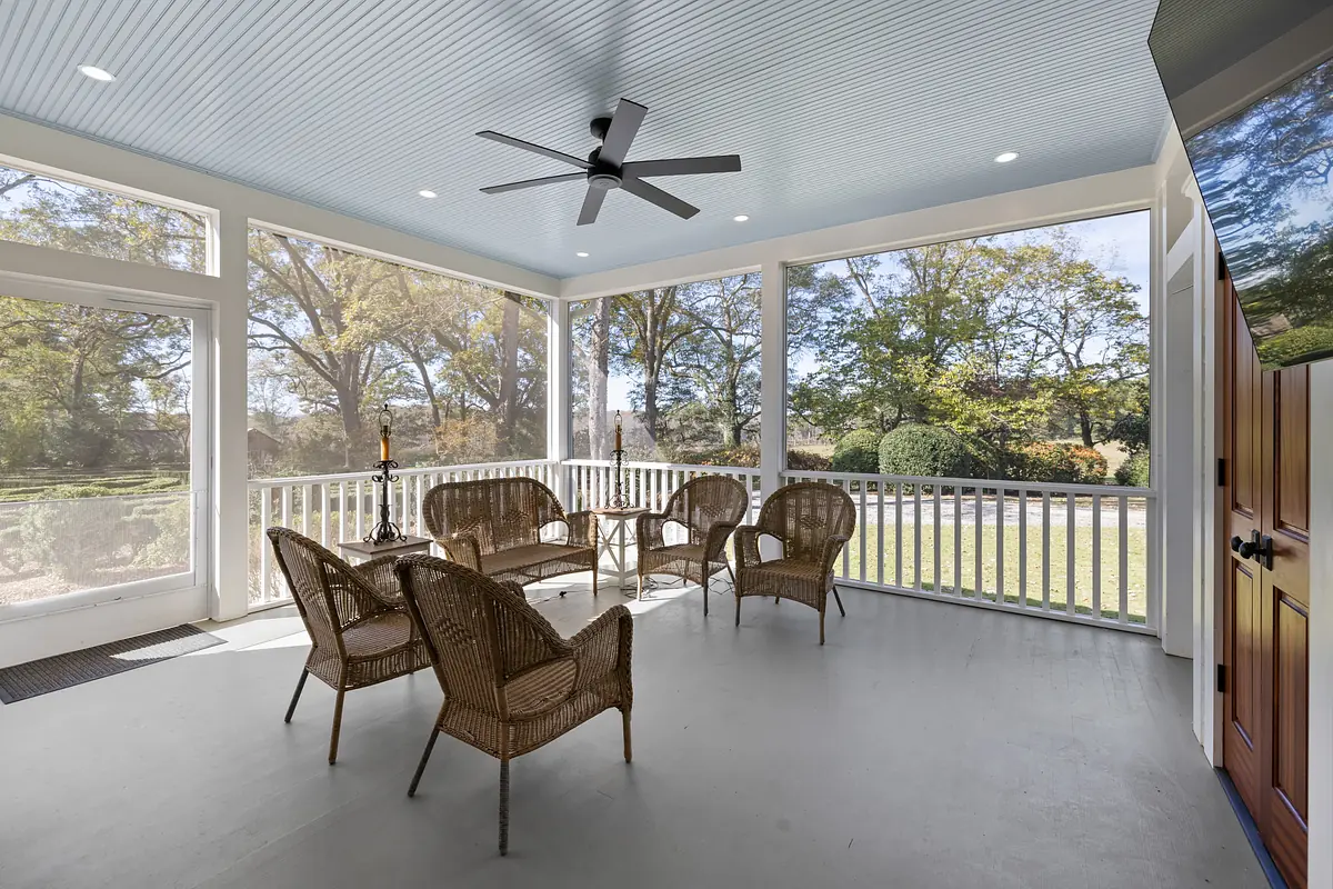 Screened-in deck with four wicker chairs, small table, light blue ceiling, and garden visibility.