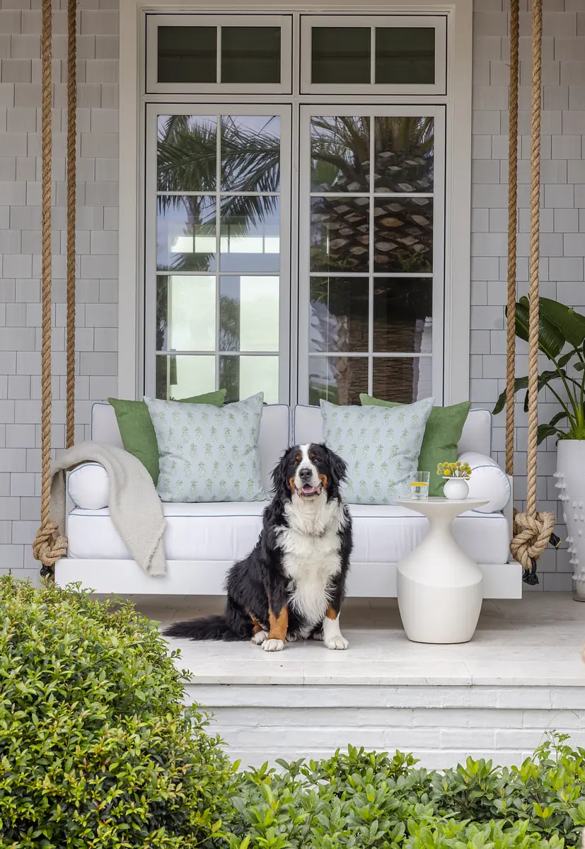 Patio with white sofa, green cushions, side table, swing, and greenery.