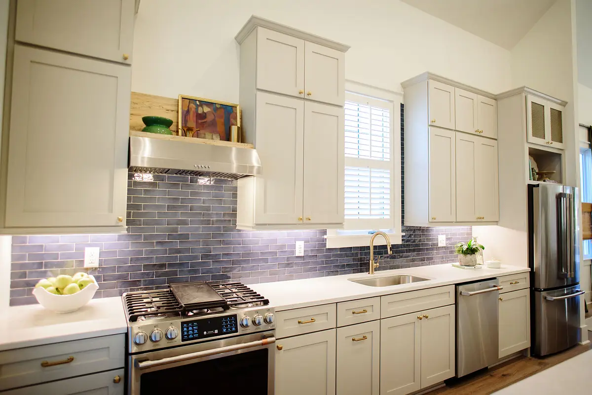 Kitchen with gray cabinets, stainless steel appliances, white countertop, and tile backsplash with natural light