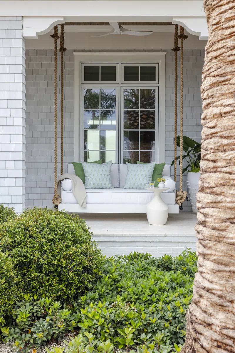 Patio with white couch, green cushions, white side table, and surrounding greenery under a window