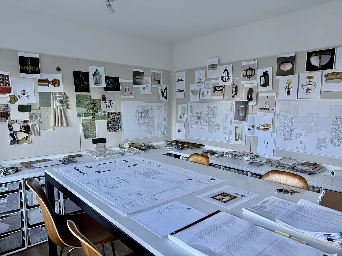 Office with black table, wooden chairs, design sketches, blueprints, and natural light from a window