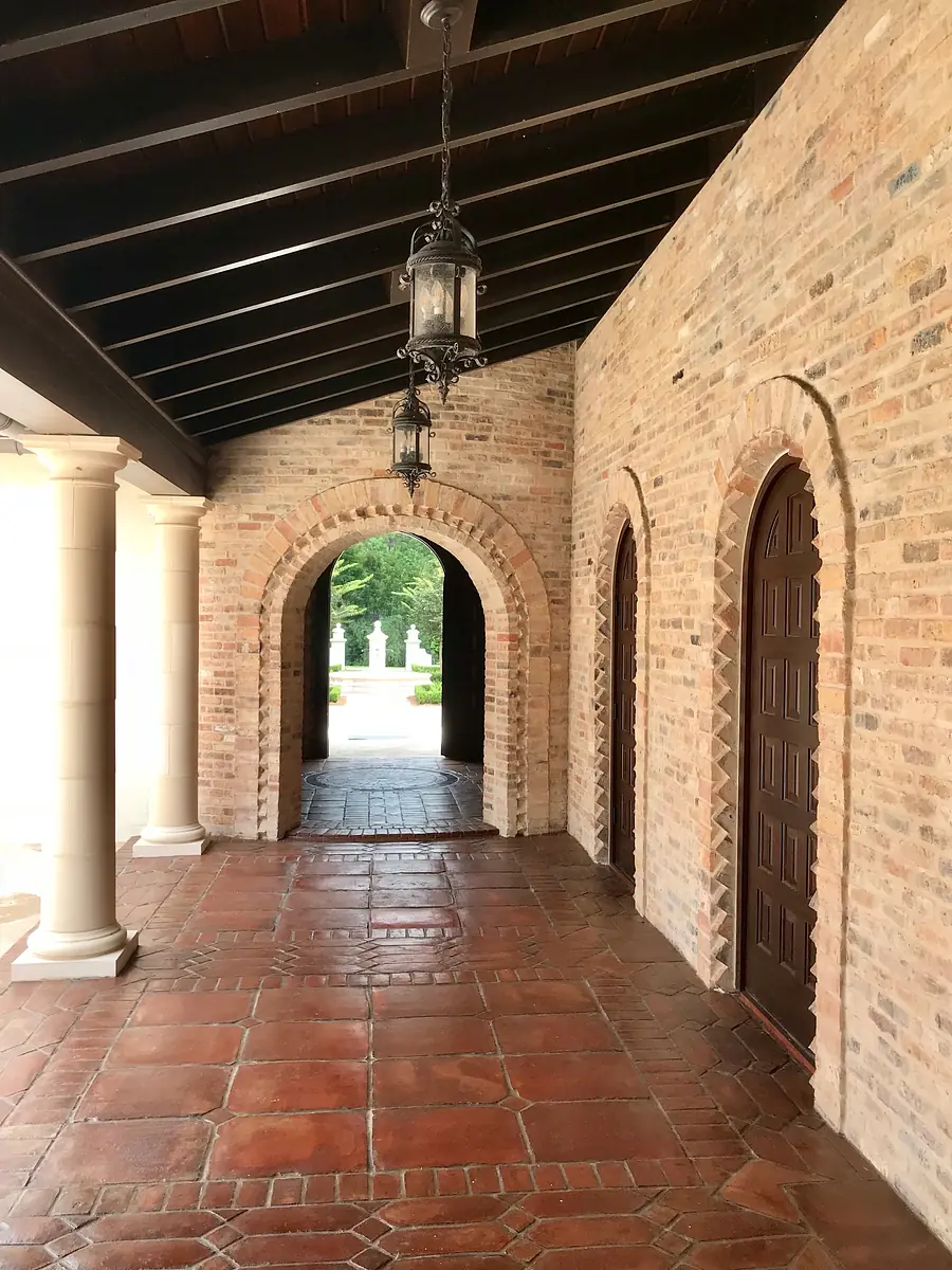 Hallway with brick walls, terracotta flooring, arched doorways, wooden doors, and lantern fixtures