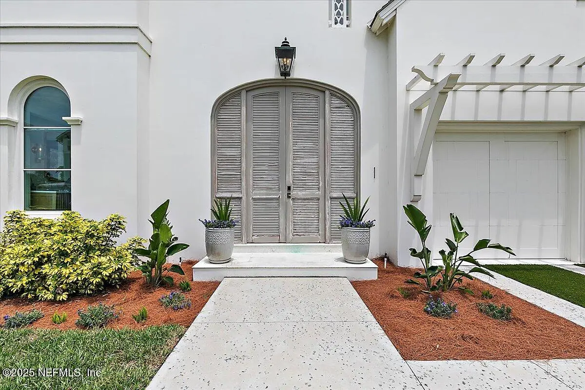 Exterior front view with double doors, potted plants, concrete pathway, and landscaped areas.