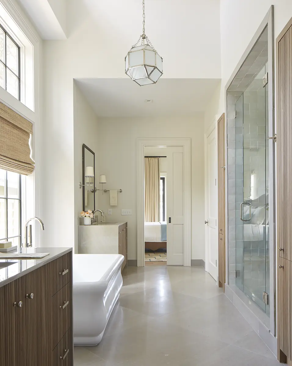 Bathroom with freestanding tub, wood vanity, glass shower, and natural light from windows with roller shades.