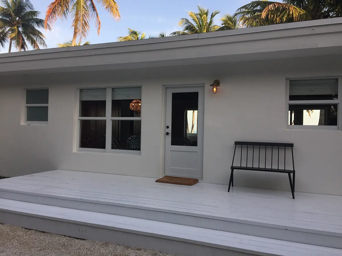 Exterior front with white building, door, windows, black bench, welcome mat, and palm trees.