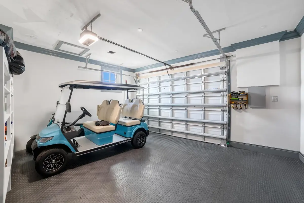 Garage with blue and white golf cart, rubber flooring, storage hooks, and overhead garage door.