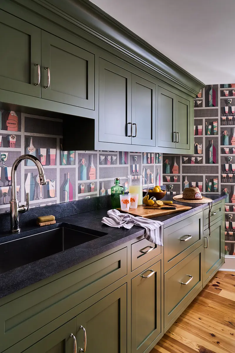 Kitchen with green cabinetry, black countertop, sink, and colorful bottle wallpaper.