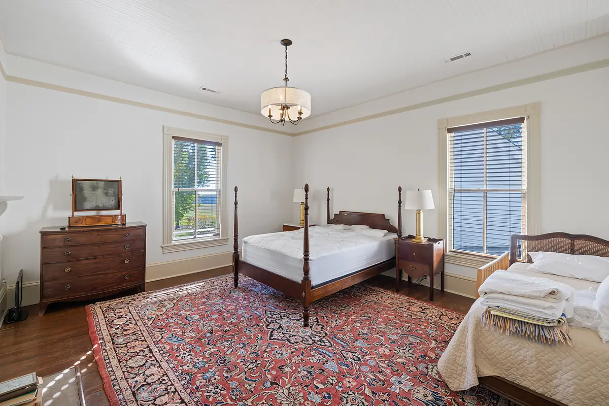 Bedroom with four-poster bed, area rug, nightstand, dresser, and two windows