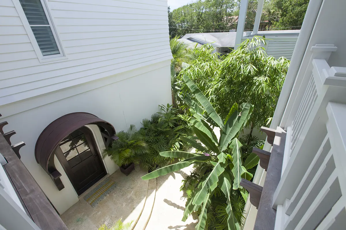 Exterior front with brown arch doorway, tropical plants, and paved pathway.