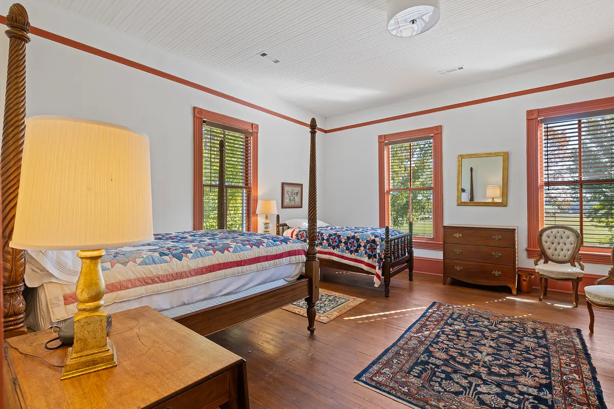 Bedroom with two four-poster beds, a nightstand, dresser, and decorative area rug with white walls and red trim.